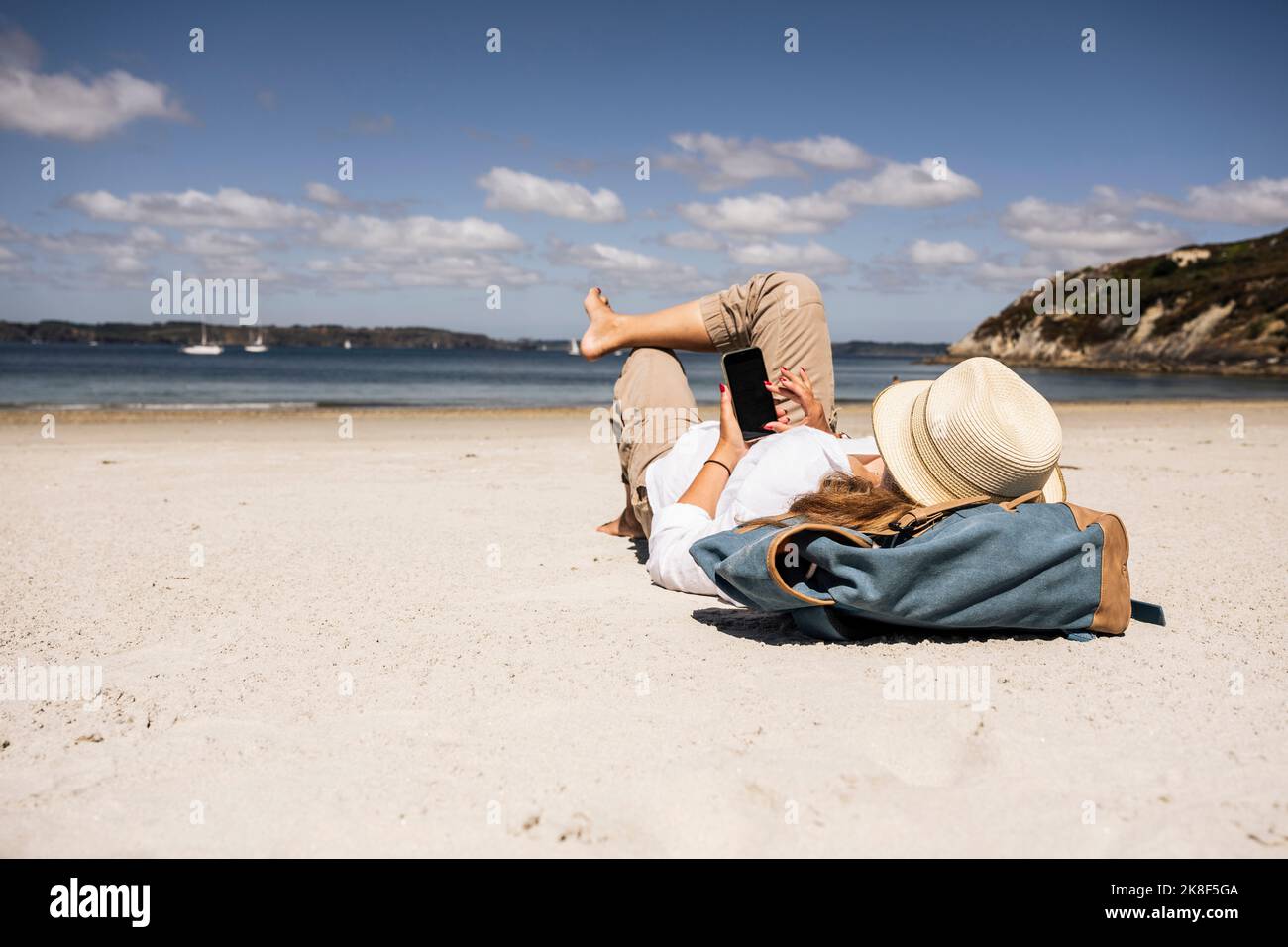 Woman with backpack using smart phone lying at beach Stock Photo