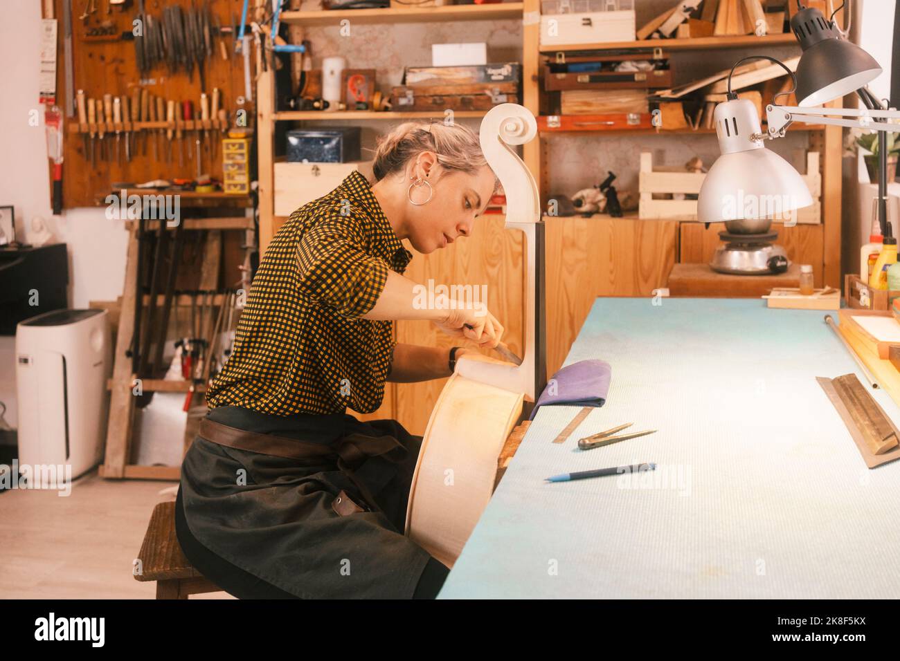Luthier with hand tool carving on double bass at Stock Photo