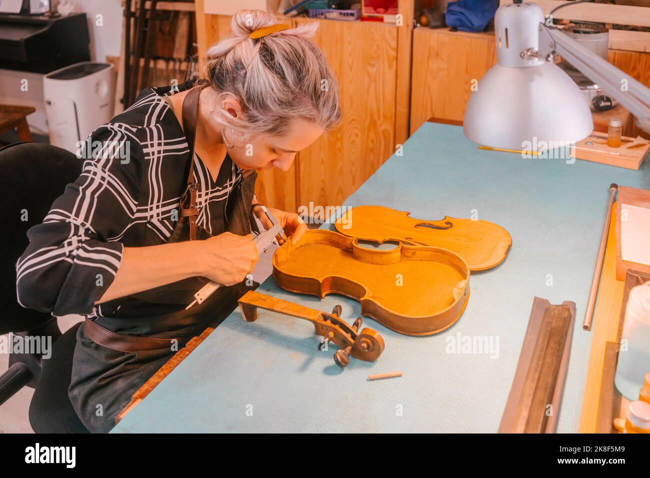 Instrument maker with tool carving and repairing violin at desk in