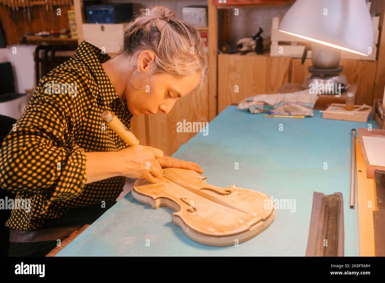 Luthier with hand tool carving on violin at desk in Stock Photo Alamy