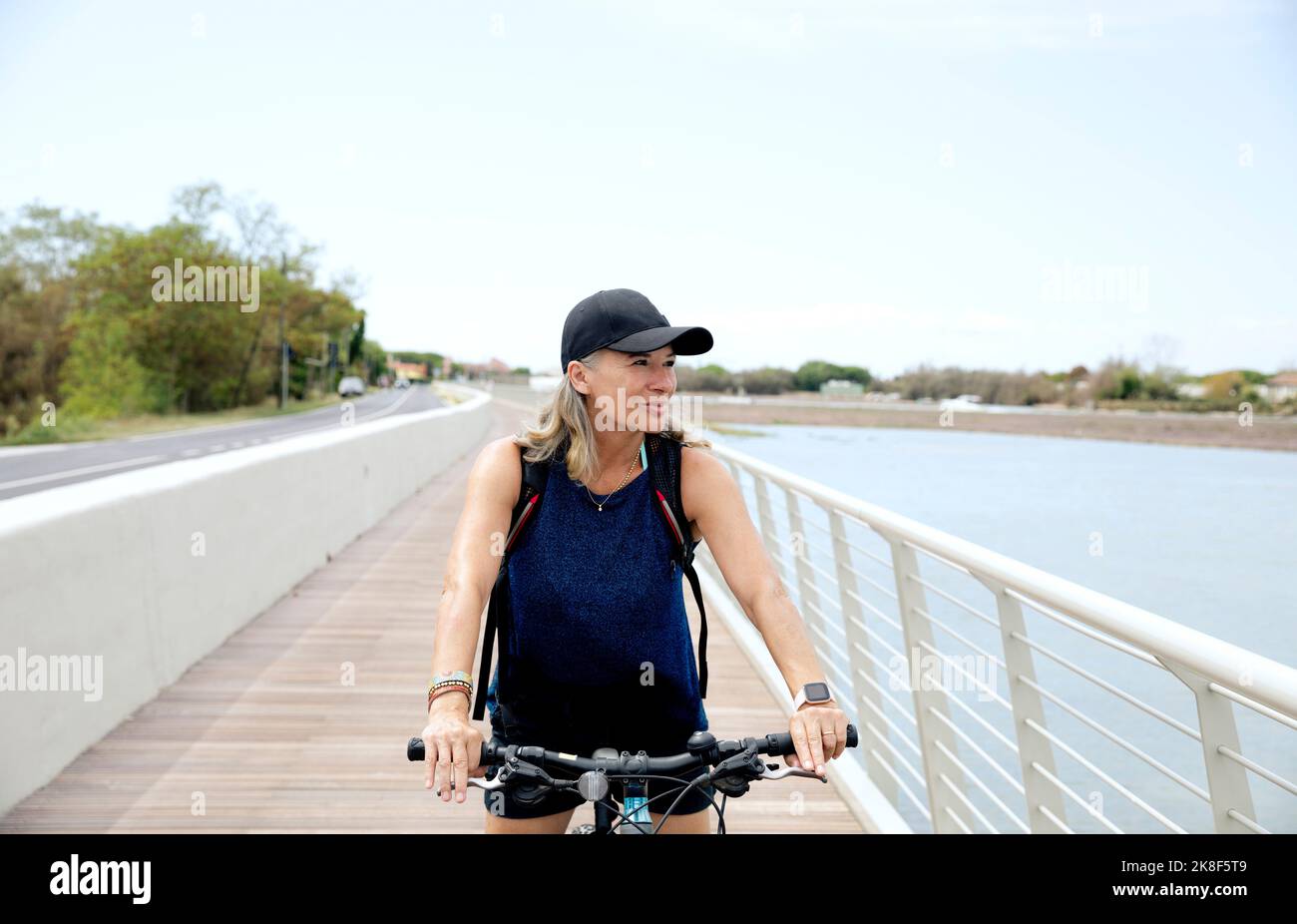 Smiling senior woman wearing cap cycling on promenade Stock Photo