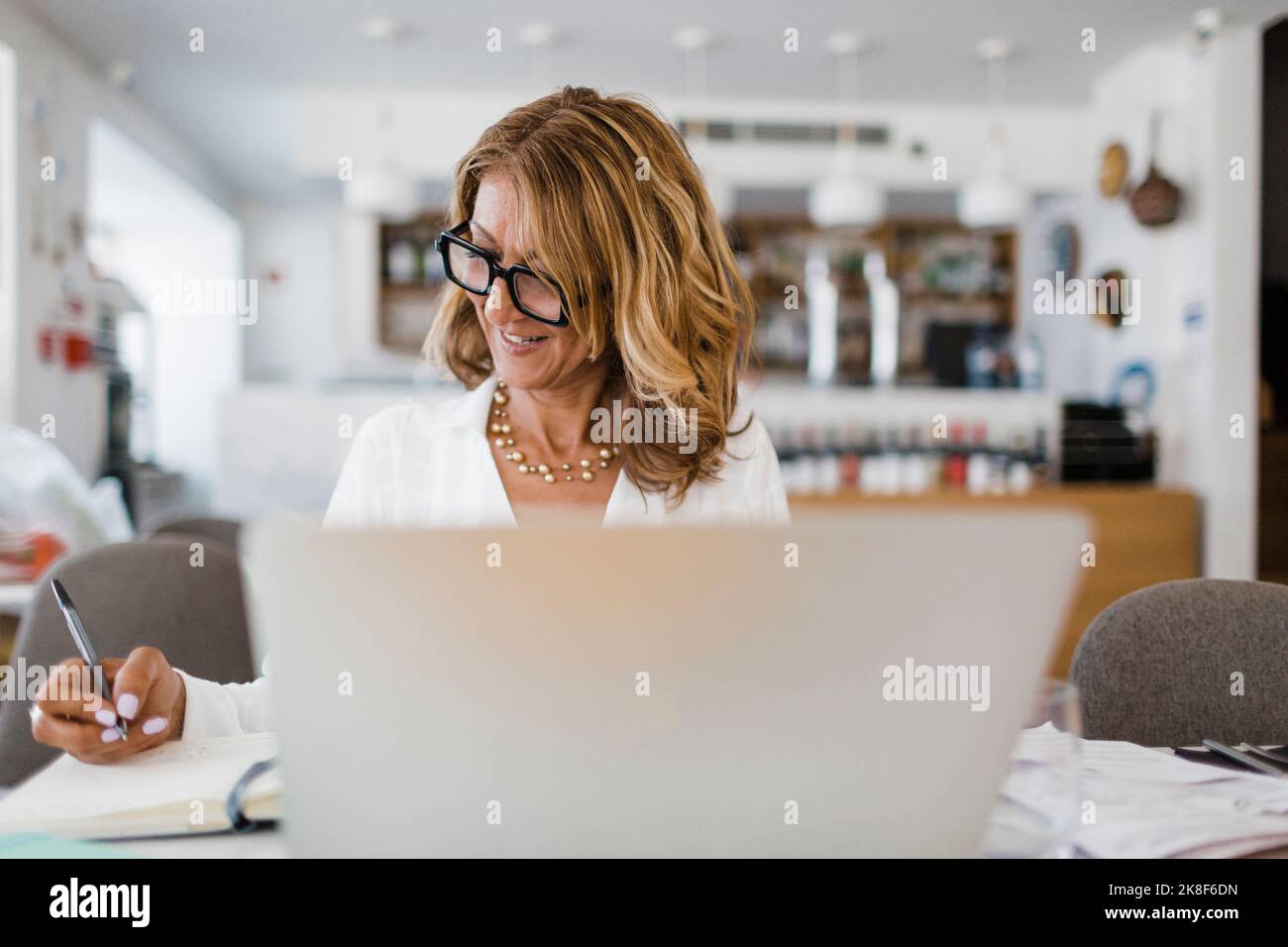 Smiling businesswoman with pen writing on diary sitting at table in restaurant Stock Photo