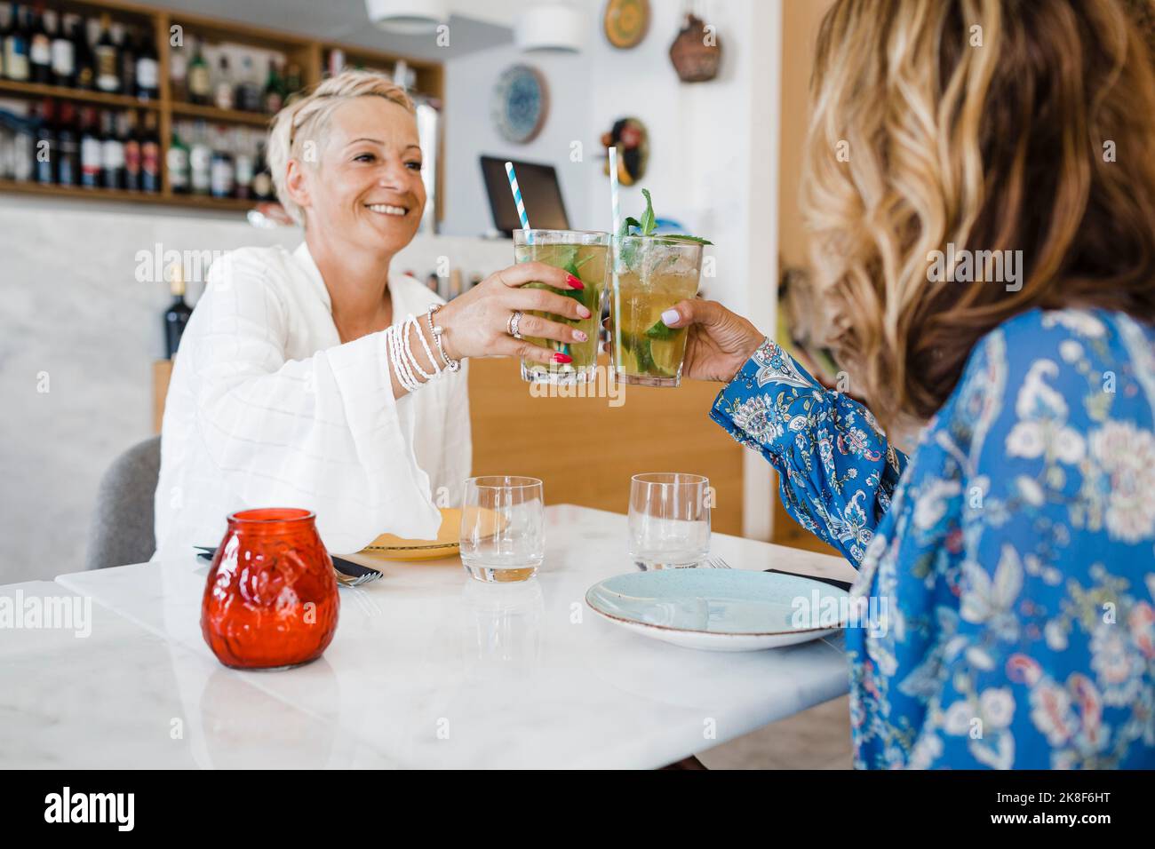 Happy friends toasting cocktail glasses at table in restaurant Stock Photo