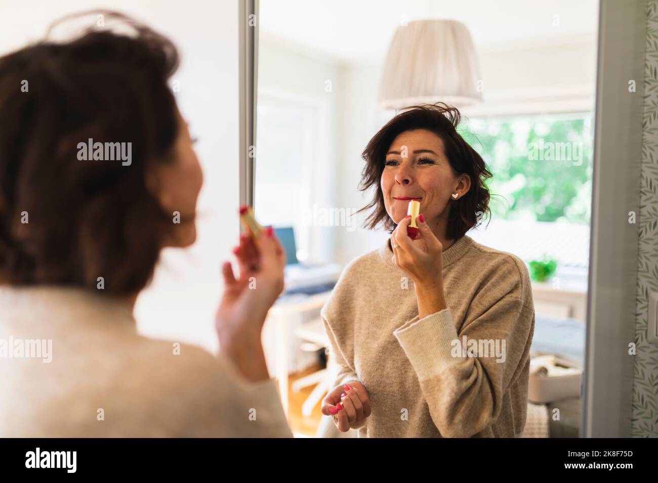 Mature woman looking in mirror and applying lipstick Stock Photo