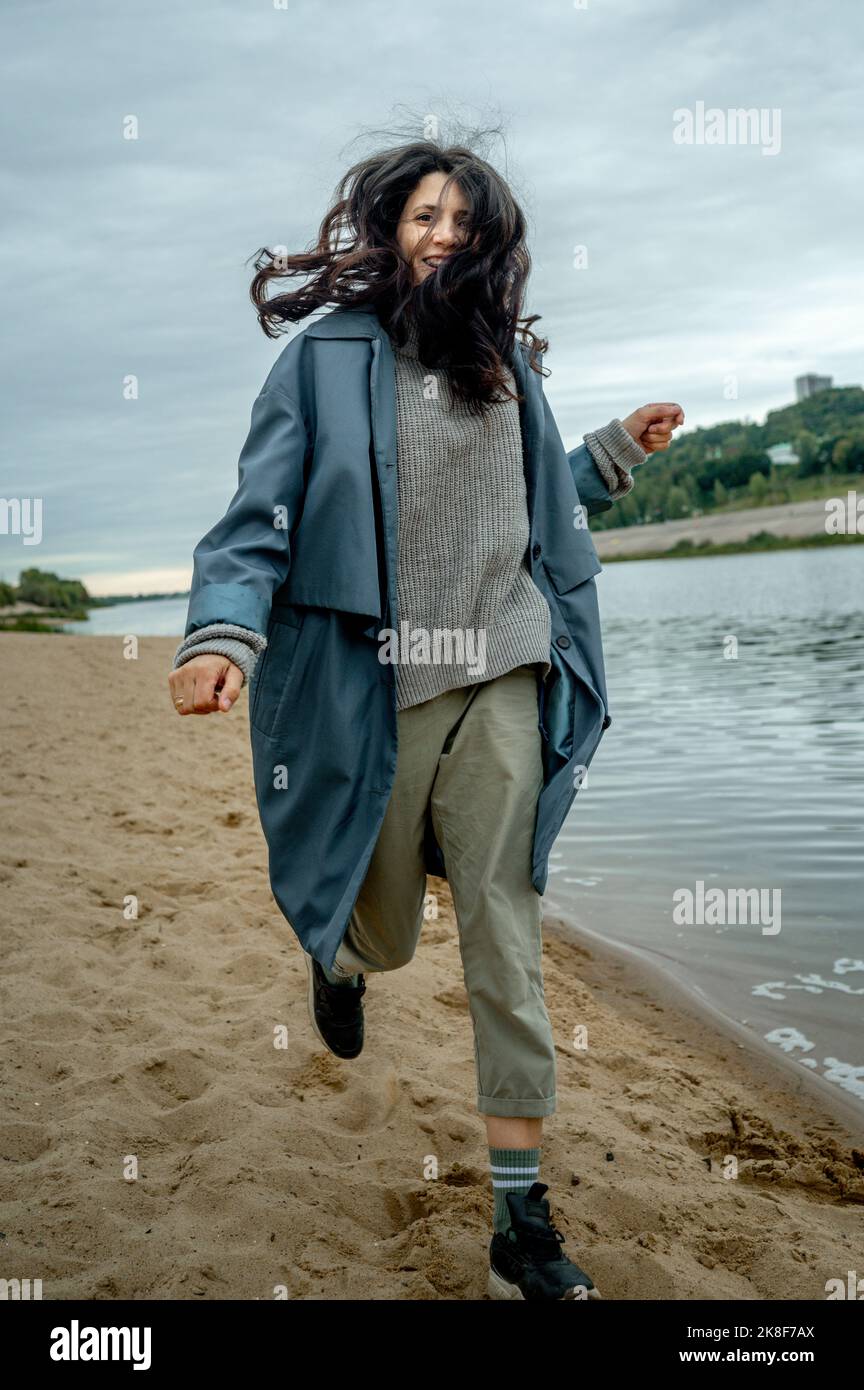 Happy woman wearing blue raincoat running at shore Stock Photo