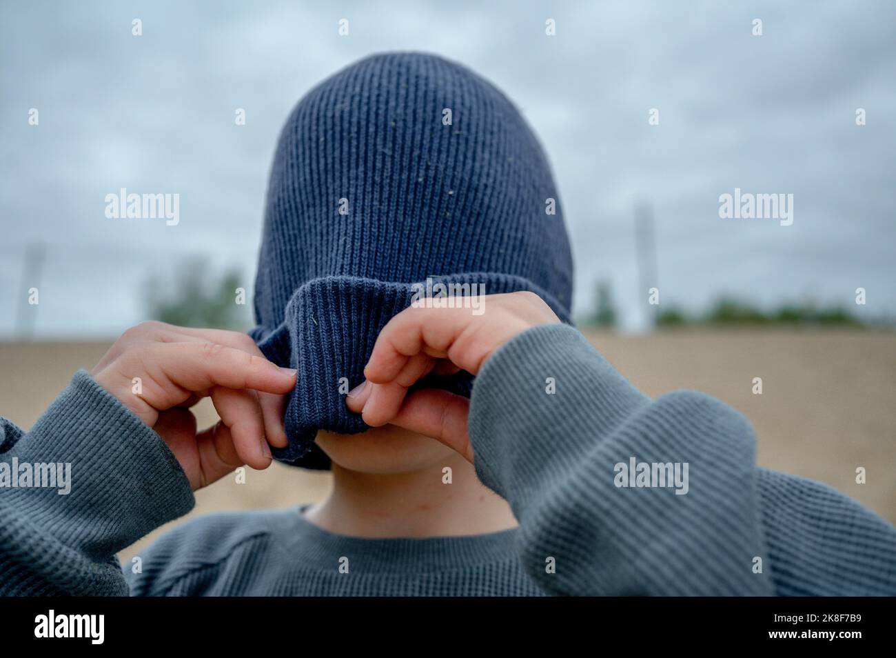 Playful boy covering face with knit hat Stock Photo