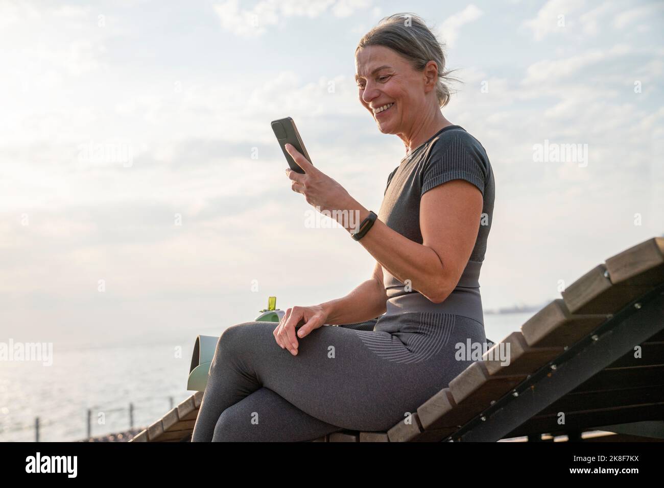 Happy woman looking at mobile phone on wooden bench Stock Photo