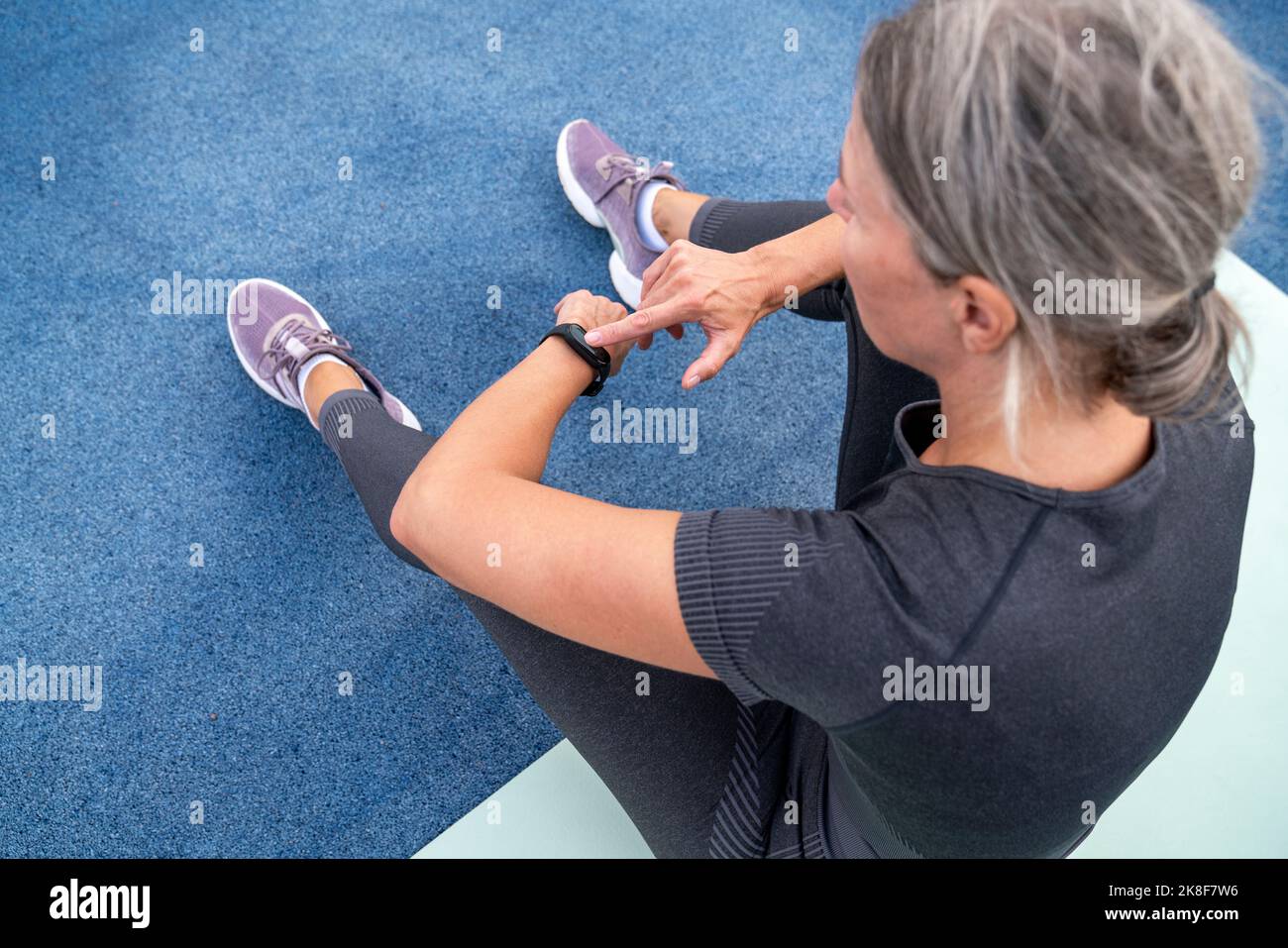 Mature woman checking time in smart watch sitting on exercise mat Stock Photo