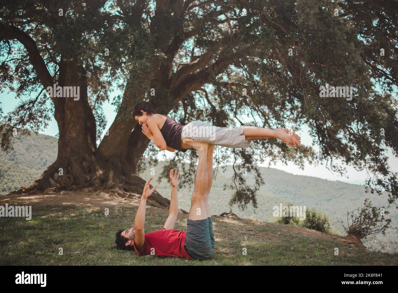 Young couple practicing acroyoga under oak tree Stock Photo
