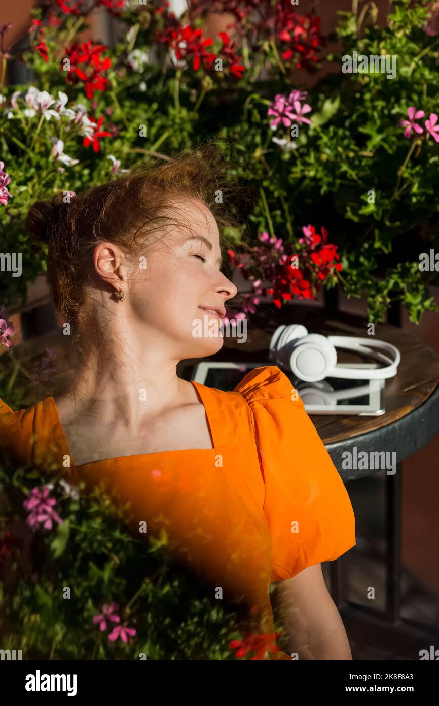 Smiling woman with eyes closed in front of flowering plant Stock Photo