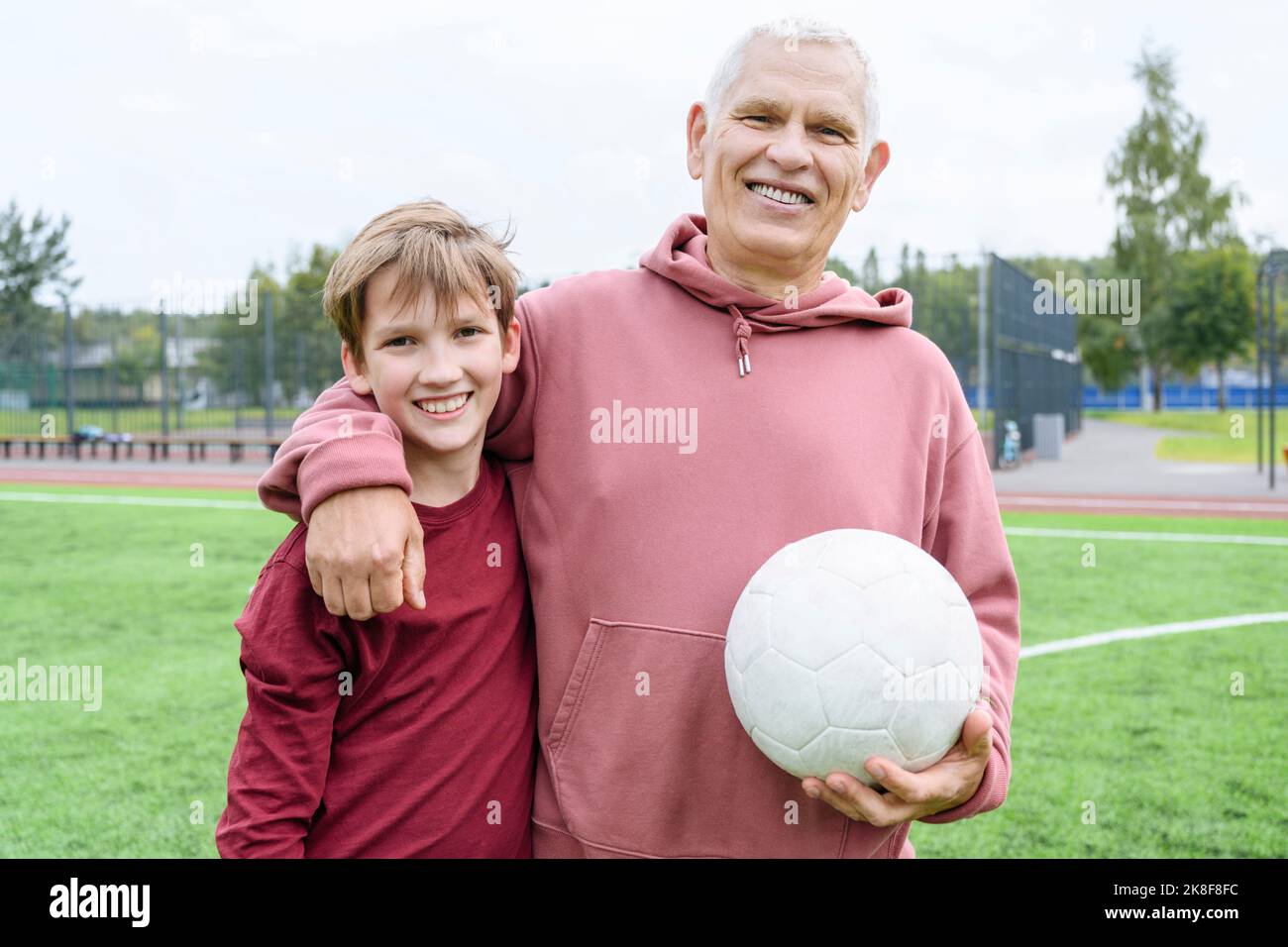 Smiling retired senior man holding soccer ball with arm around grandson Stock Photo