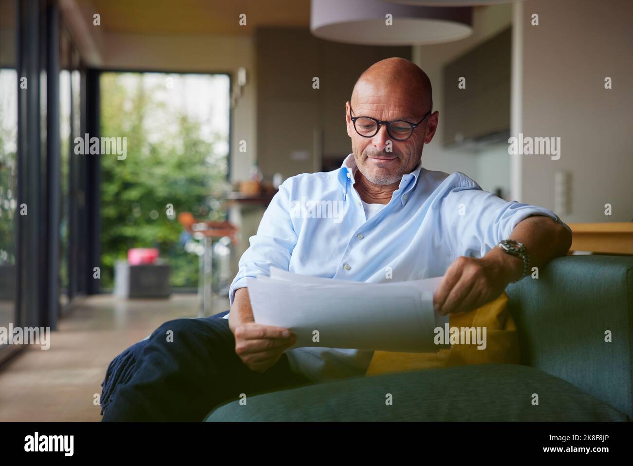 Senior man reading documents sitting on sofa at home Stock Photo