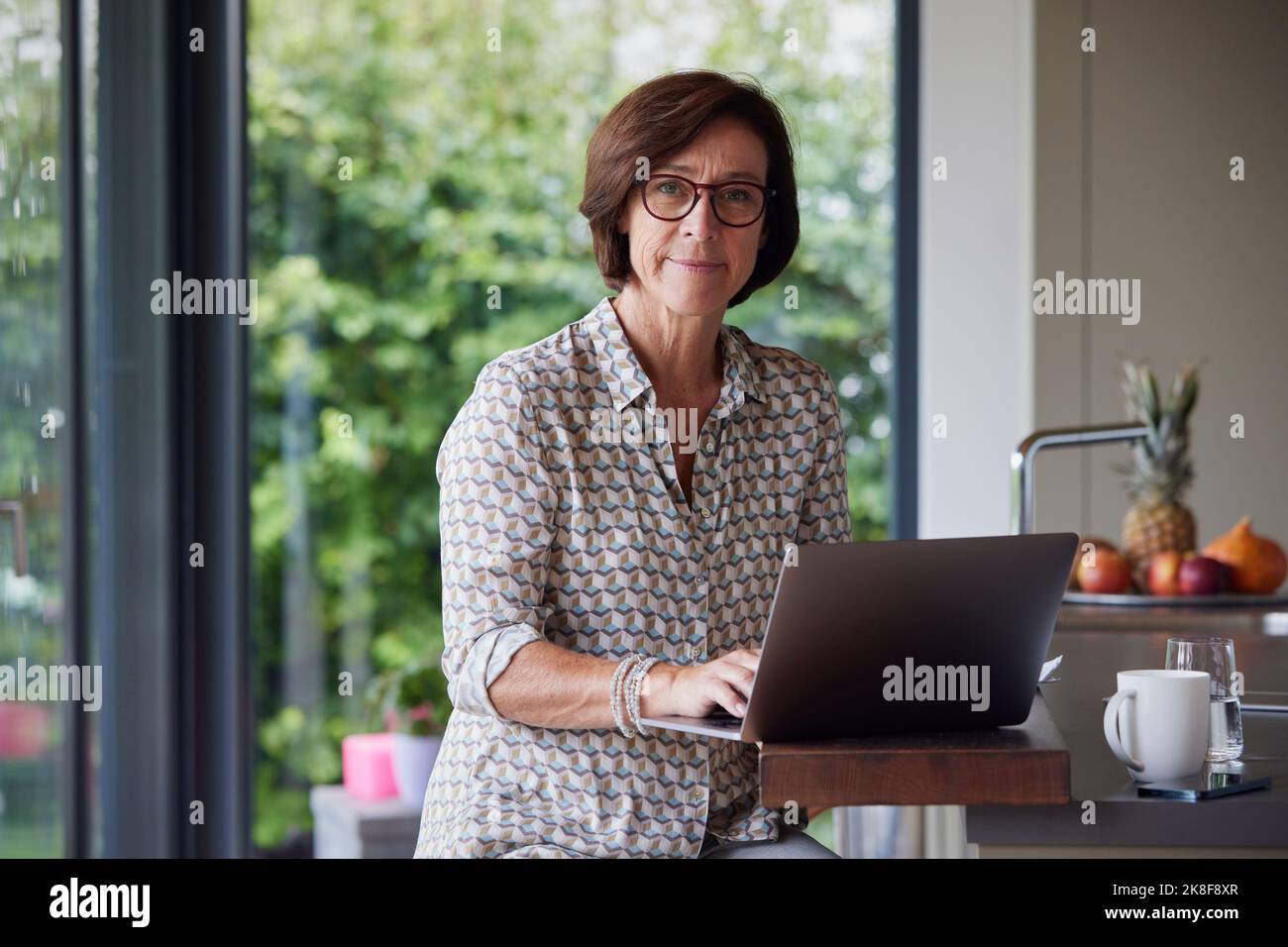 Senior woman with laptop sitting at kitchen island Stock Photo