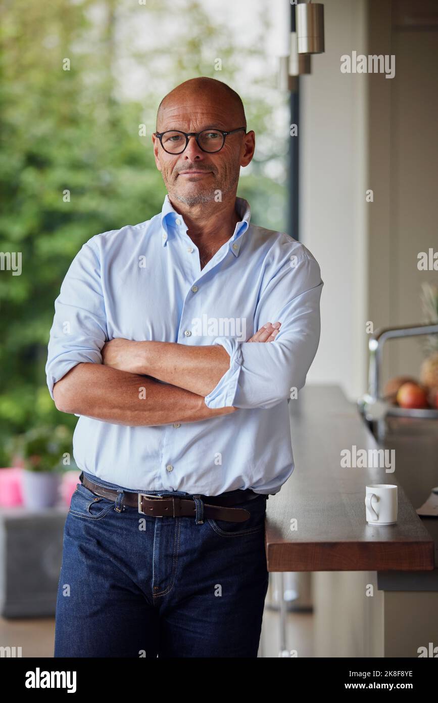 Senior man with arms crossed standing by kitchen island at home Stock Photo