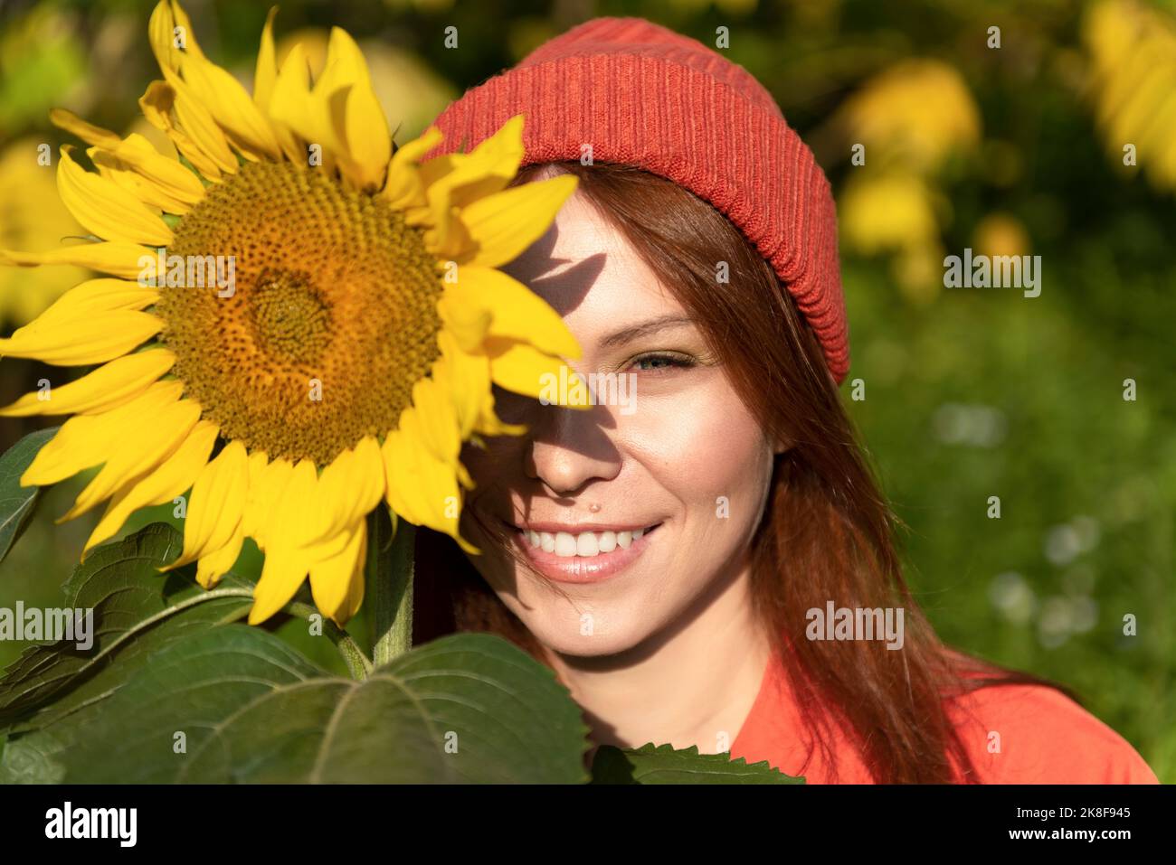 Smiling woman wearing knit hat holding sunflower on sunny day Stock Photo