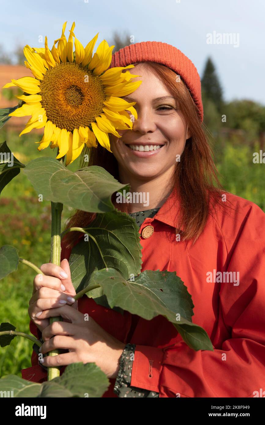 Smiling woman with brown hair holding sunflower in garden Stock Photo
