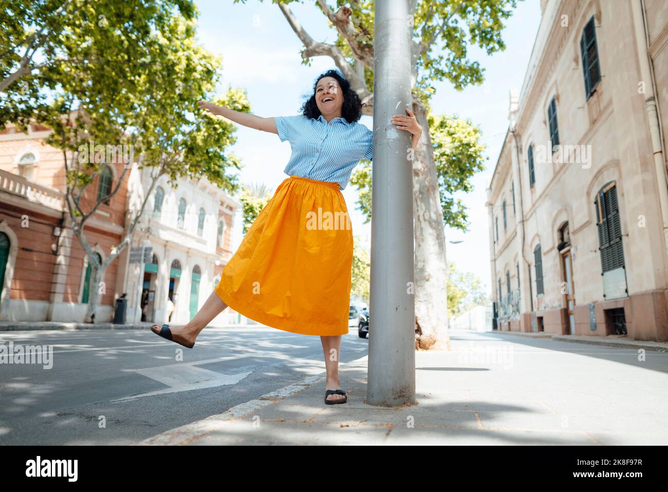 Playful woman holding pole dancing on sidewalk in city Stock Photo