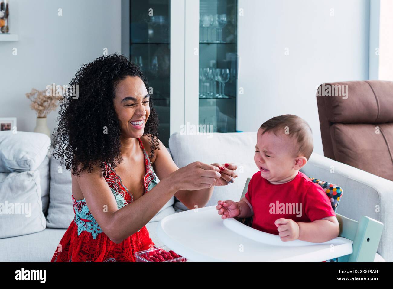 Happy mother with crying baby boy sitting in high chair at home Stock Photo
