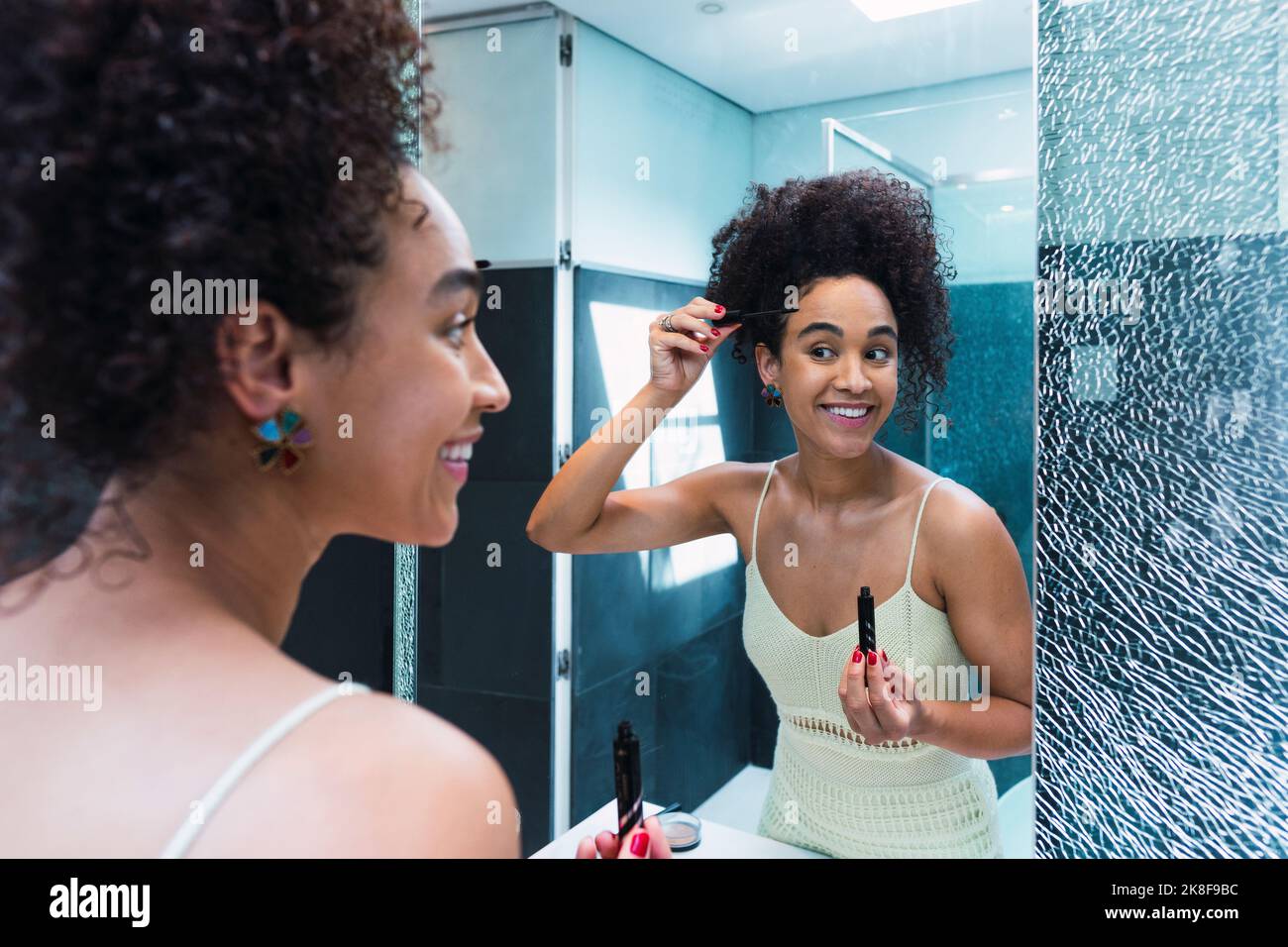 Happy woman doing make-up standing in front of mirror at home Stock Photo