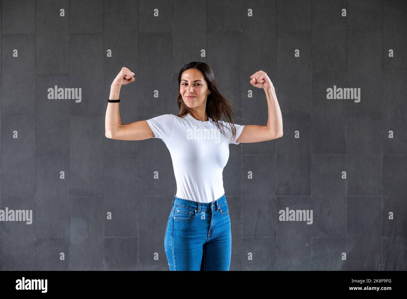 Happy woman flexing muscles in front of gray wall Stock Photo