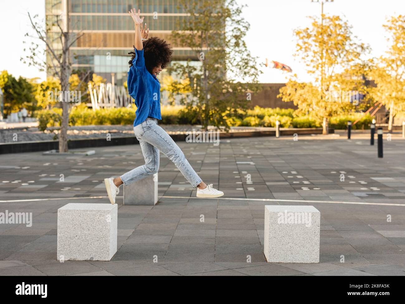 Woman with arms raised jumping on concrete block Stock Photo