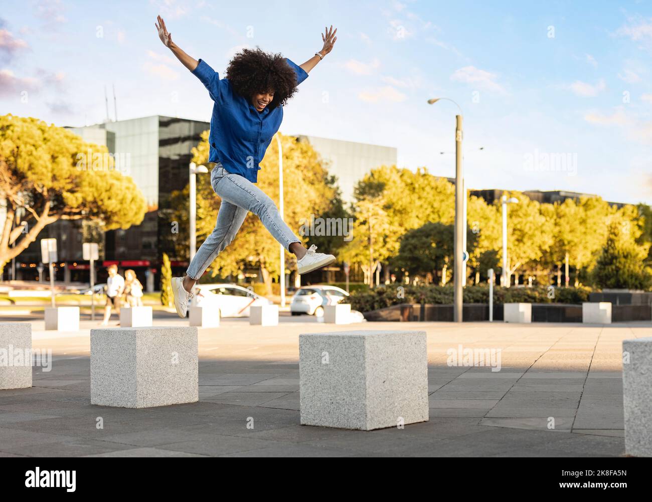Happy woman with arms raised jumping on concrete block Stock Photo