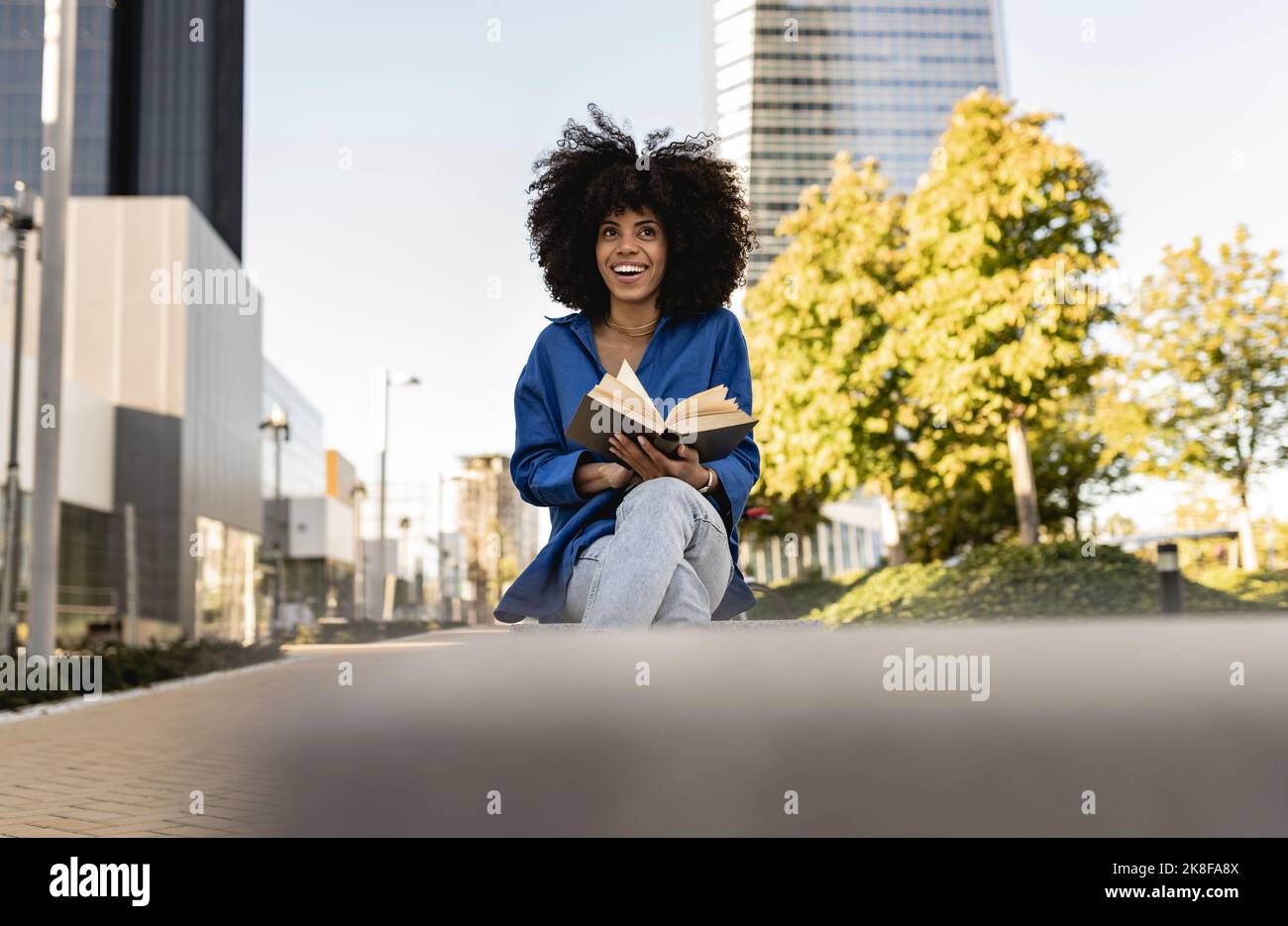 Happy woman with Afro hairstyle holding book Stock Photo - Alamy