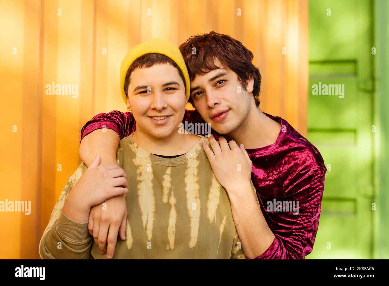 Smiling non-binary couple standing in front of yellow cargo container Stock Photo