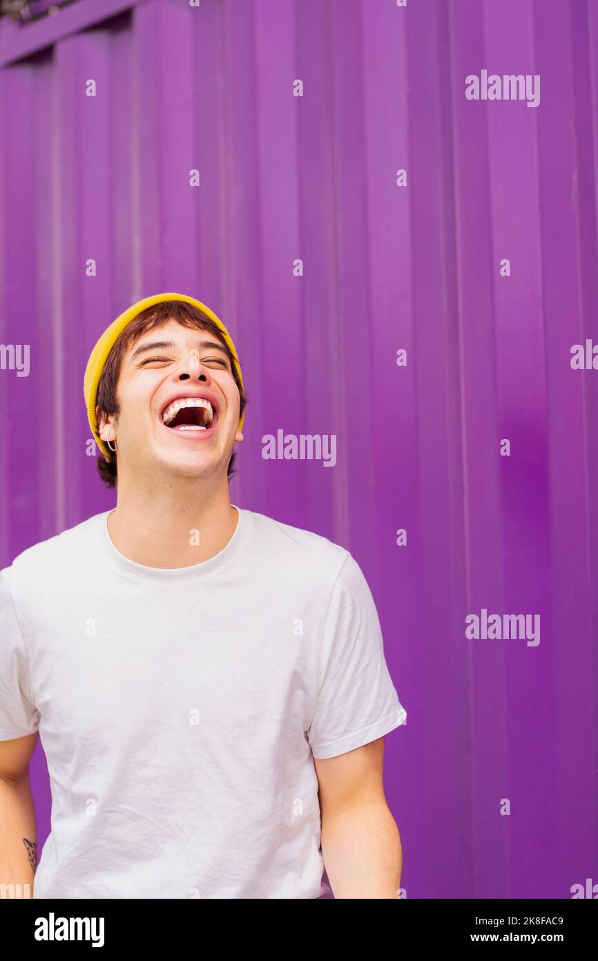 Cheerful non-binary person laughing in front of purple wall Stock Photo