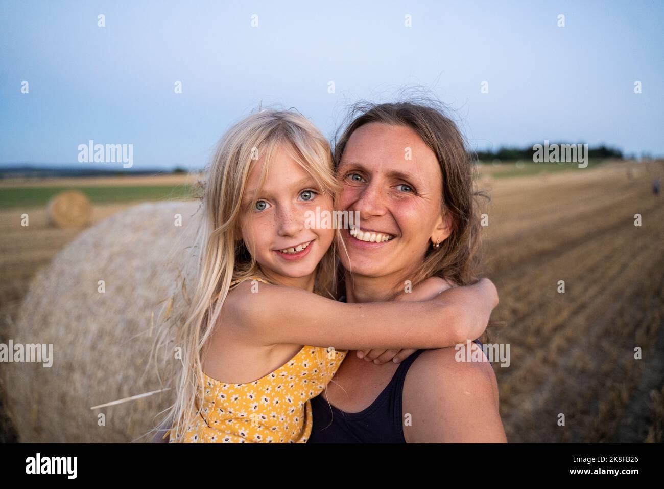 Smiling girl with blond hair embracing mother at field Stock Photo
