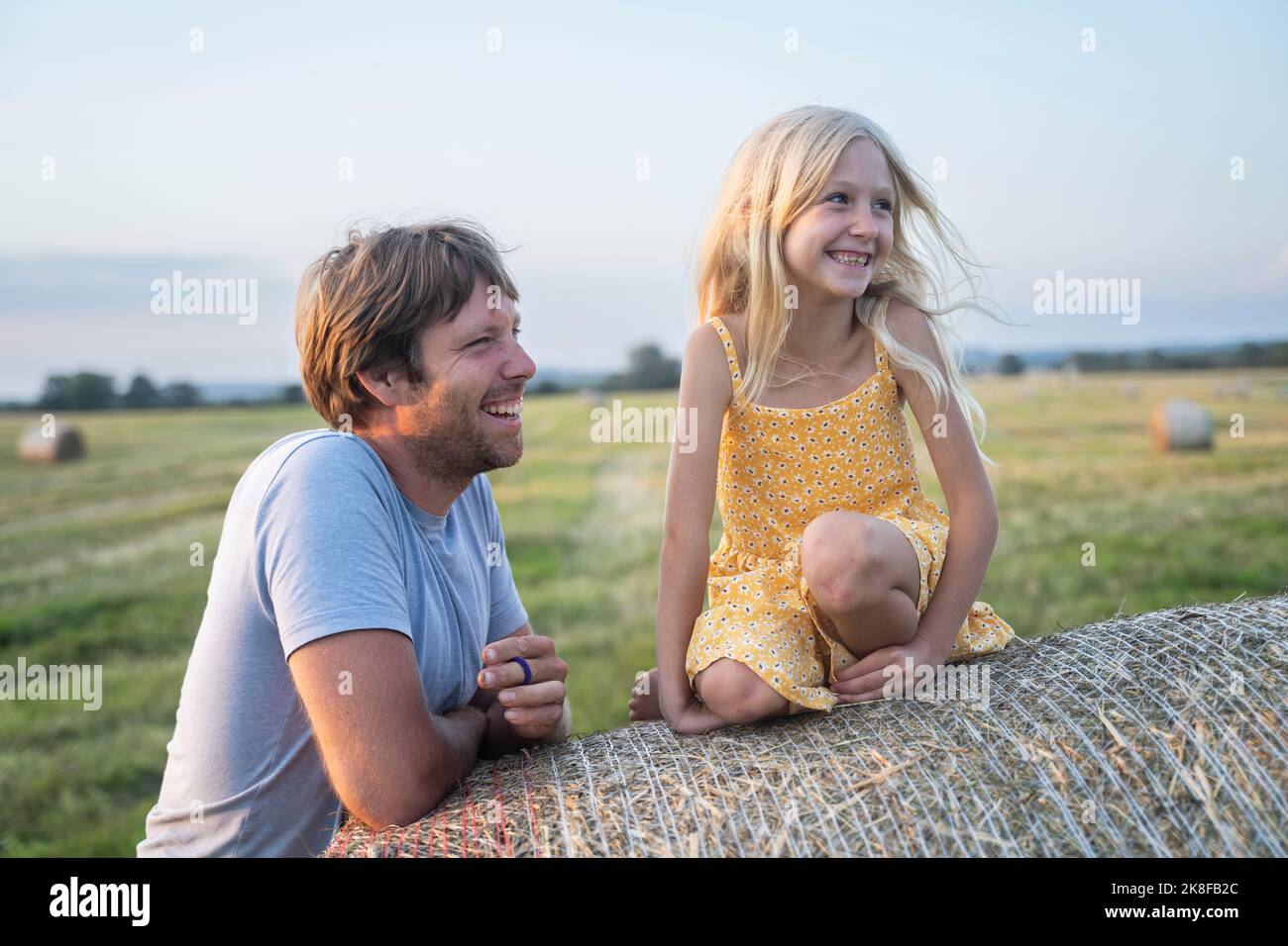 Happy man standing by girl sitting on haystack Stock Photo