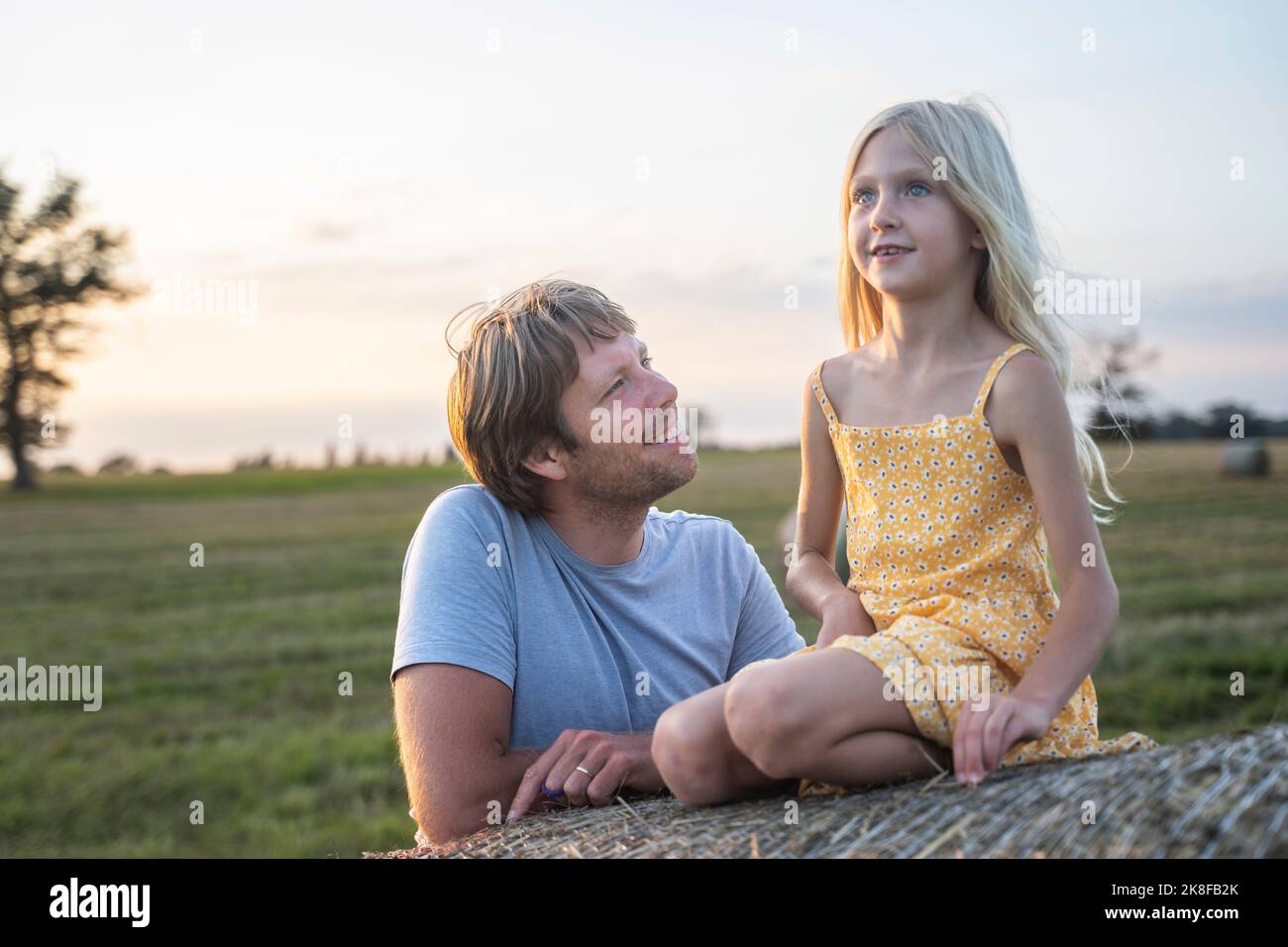 Smiling man looking at daughter sitting on haystack Stock Photo