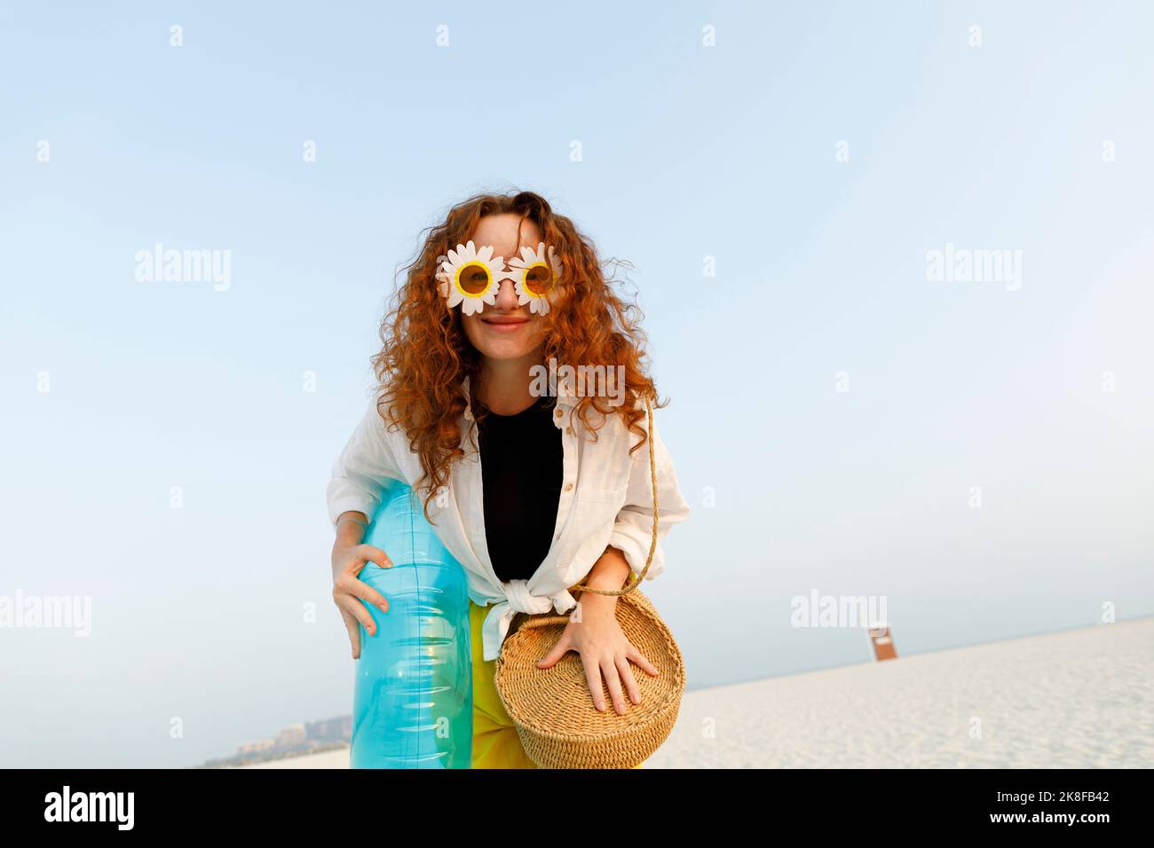Smiling woman wearing sunflower sunglasses holding blue inflatable ring at beach Stock Photo