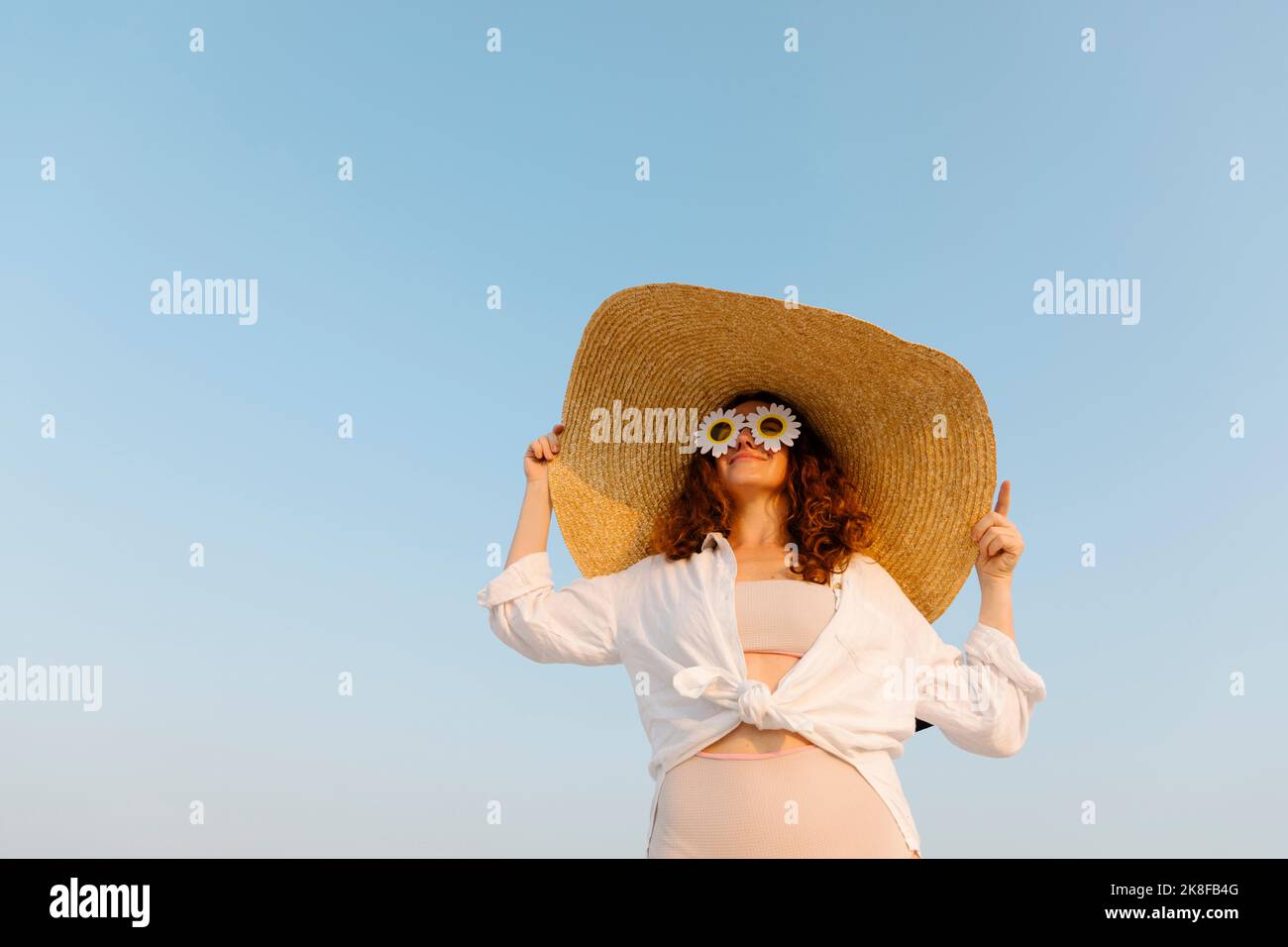 Smiling woman wearing sunflower sunglasses and oversized straw hat on sunny day Stock Photo