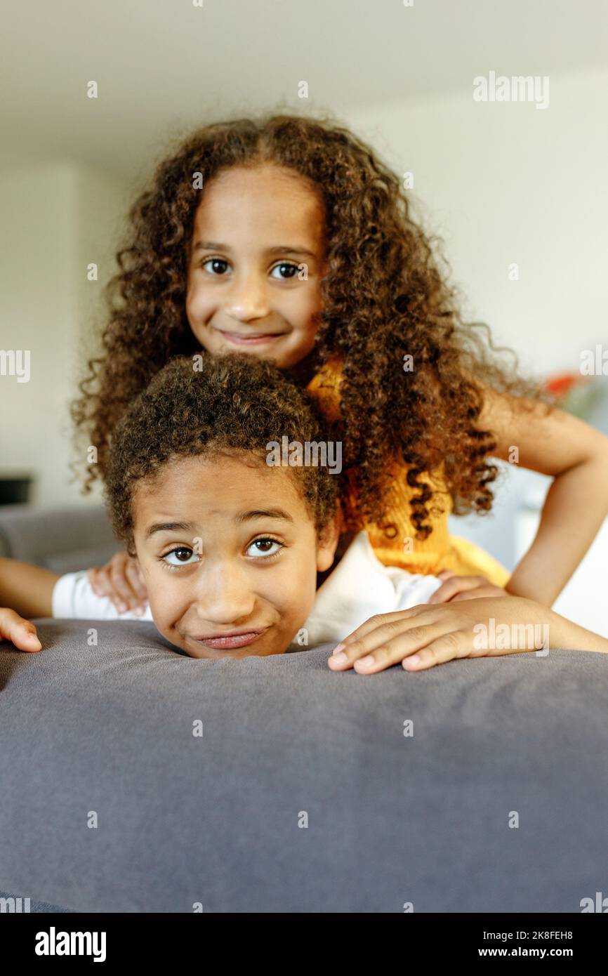 Smiling girl with curly hair leaning on brother at home Stock Photo Alamy