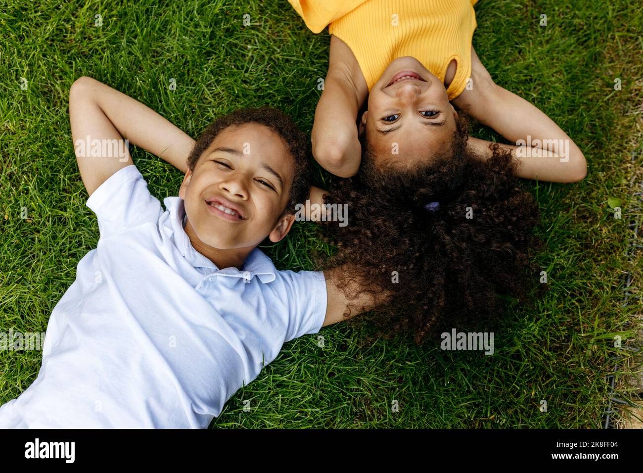 Smiling boy and girl with hands behind head lying on grass Stock Photo