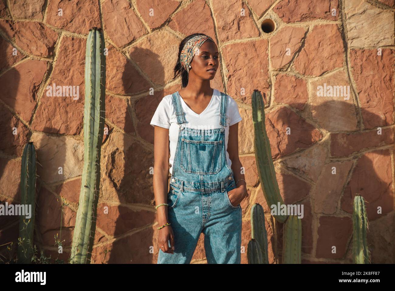 Young woman wearing bibs overall standing in front of wall Stock Photo