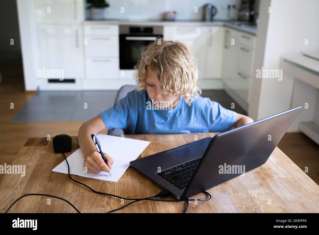 Boy doing homework with laptop on table at home Stock Photo