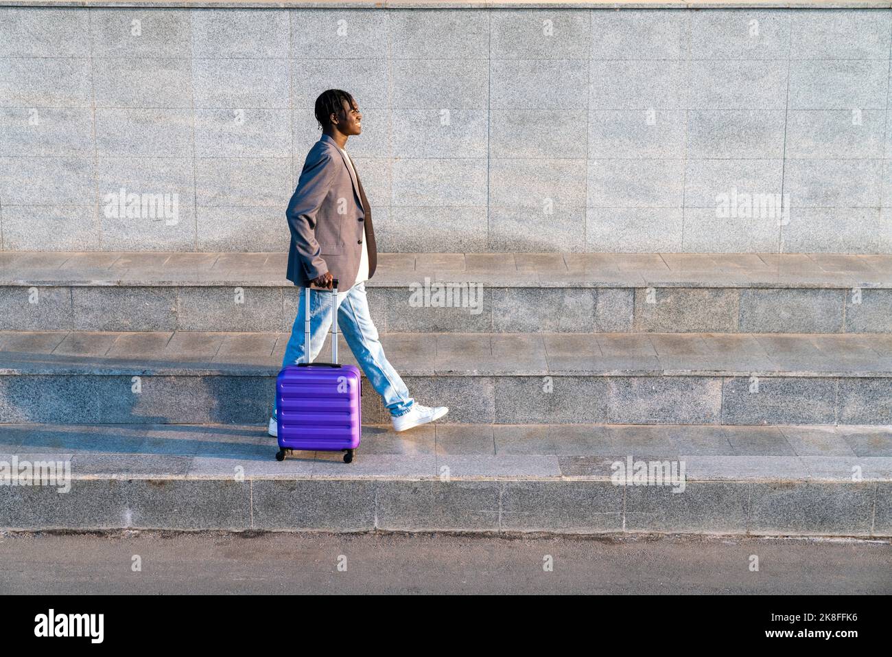 Smiling young businessman with suitcase walking on step Stock Photo