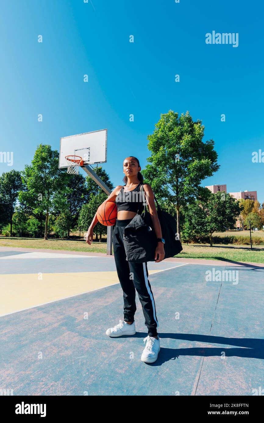 Confident sportswoman with basketball in sports court on sunny day ...