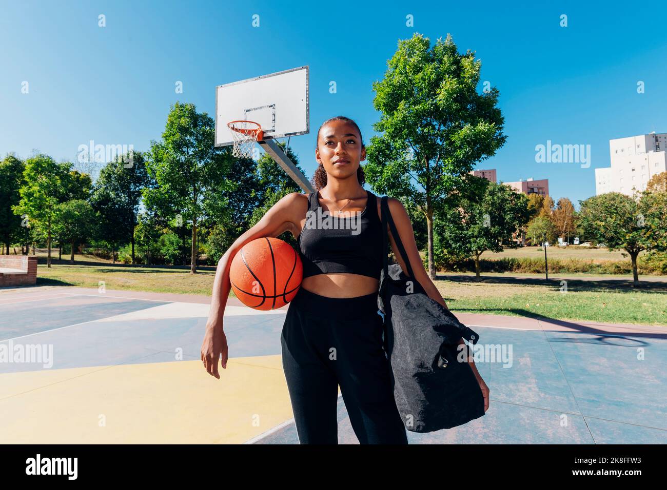 Thoughtful young sportswoman holding sports ball in basketball court ...