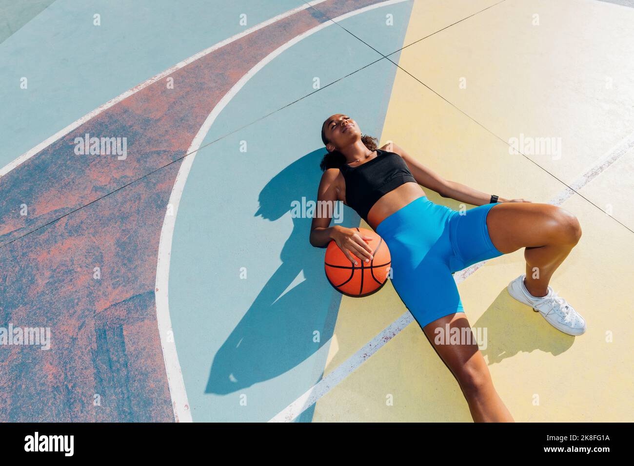 Young sportswoman relaxing with ball lying on basketball court Stock ...