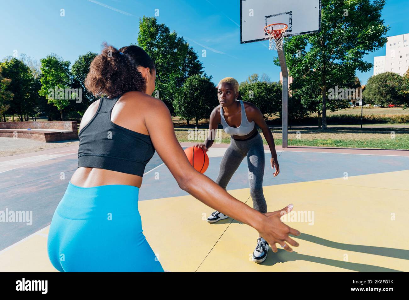 Young sportswoman dribbling basketball playing with friend in sports court Stock Photo