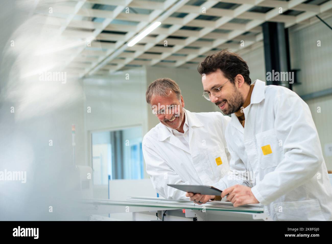 Happy engineer with colleague using tablet PC at industry Stock Photo