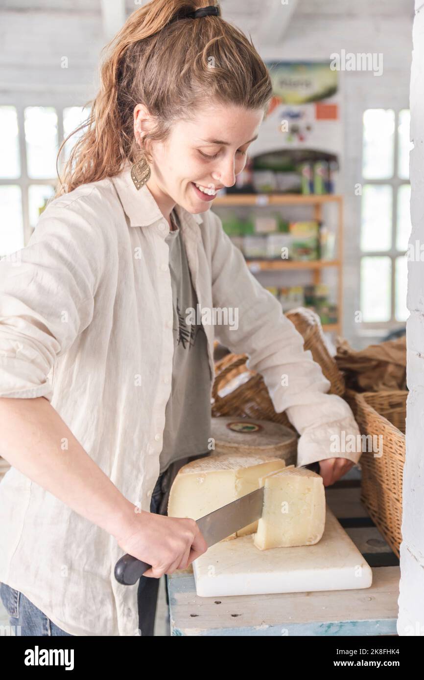 Smiling grocer cutting cheese in greengrocer shop Stock Photo