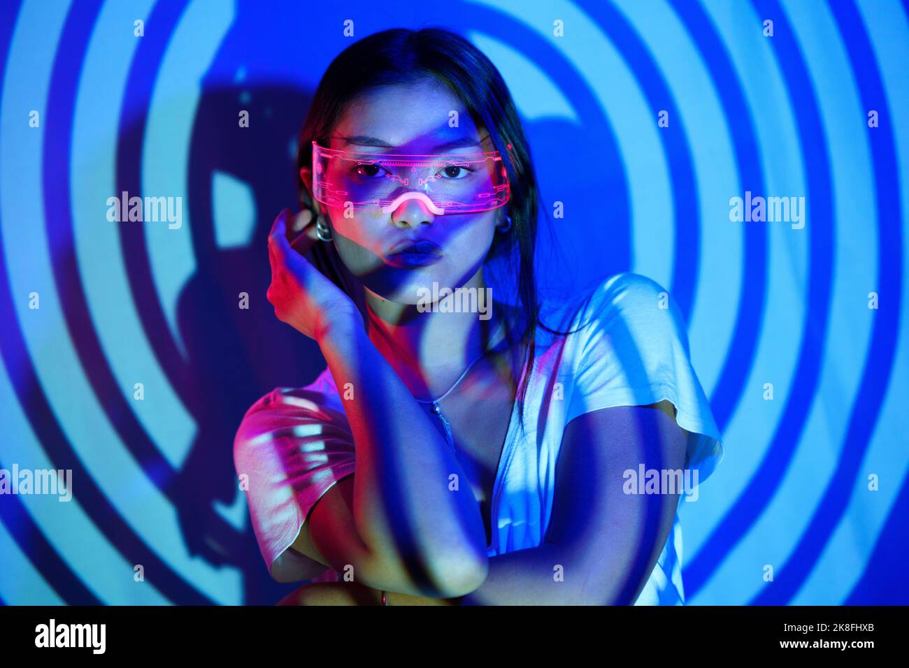 Young woman wearing LED smart glasses standing in front of wall under spiral shadow Stock Photo