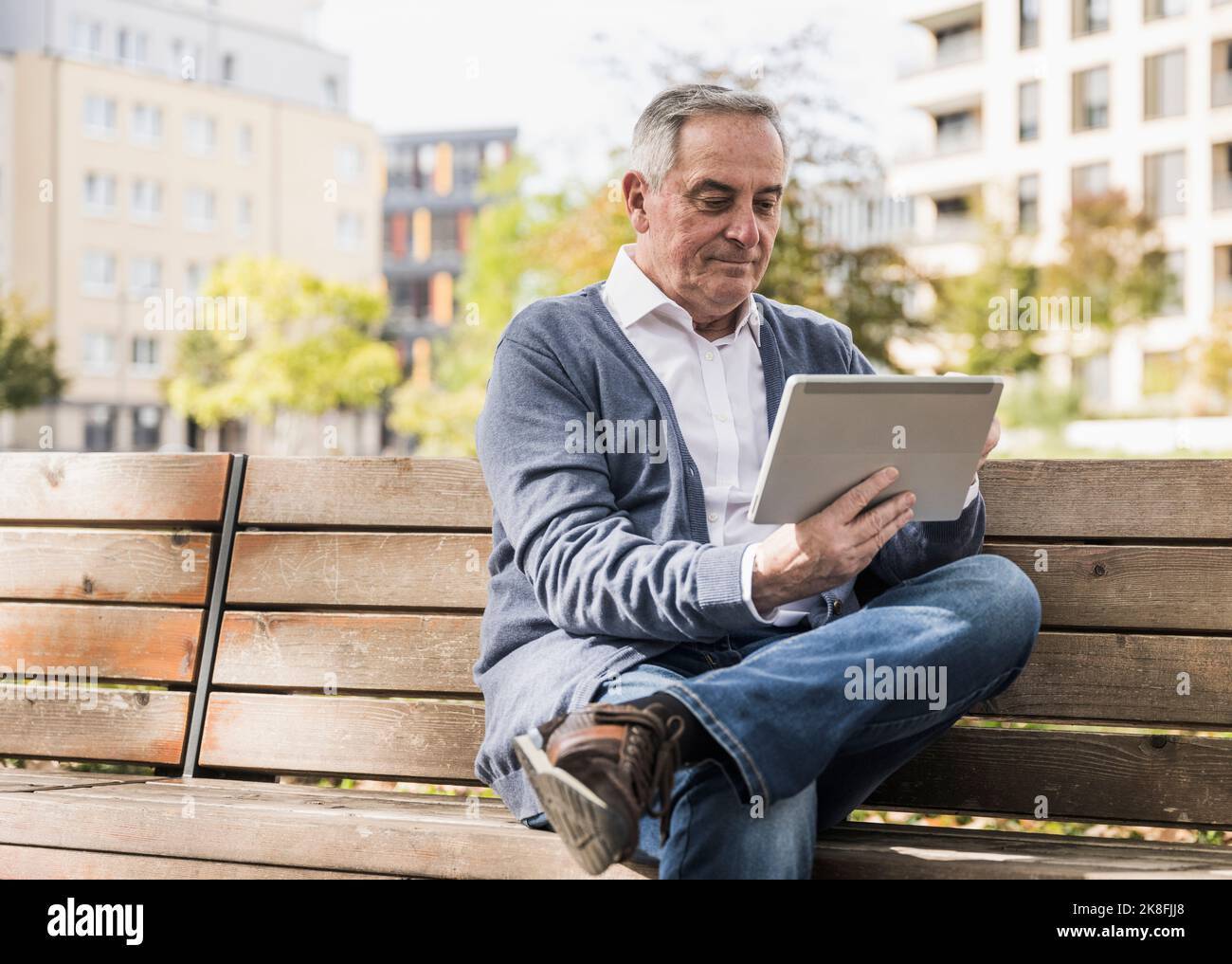 Senior man using tablet computer sitting on bench Stock Photo