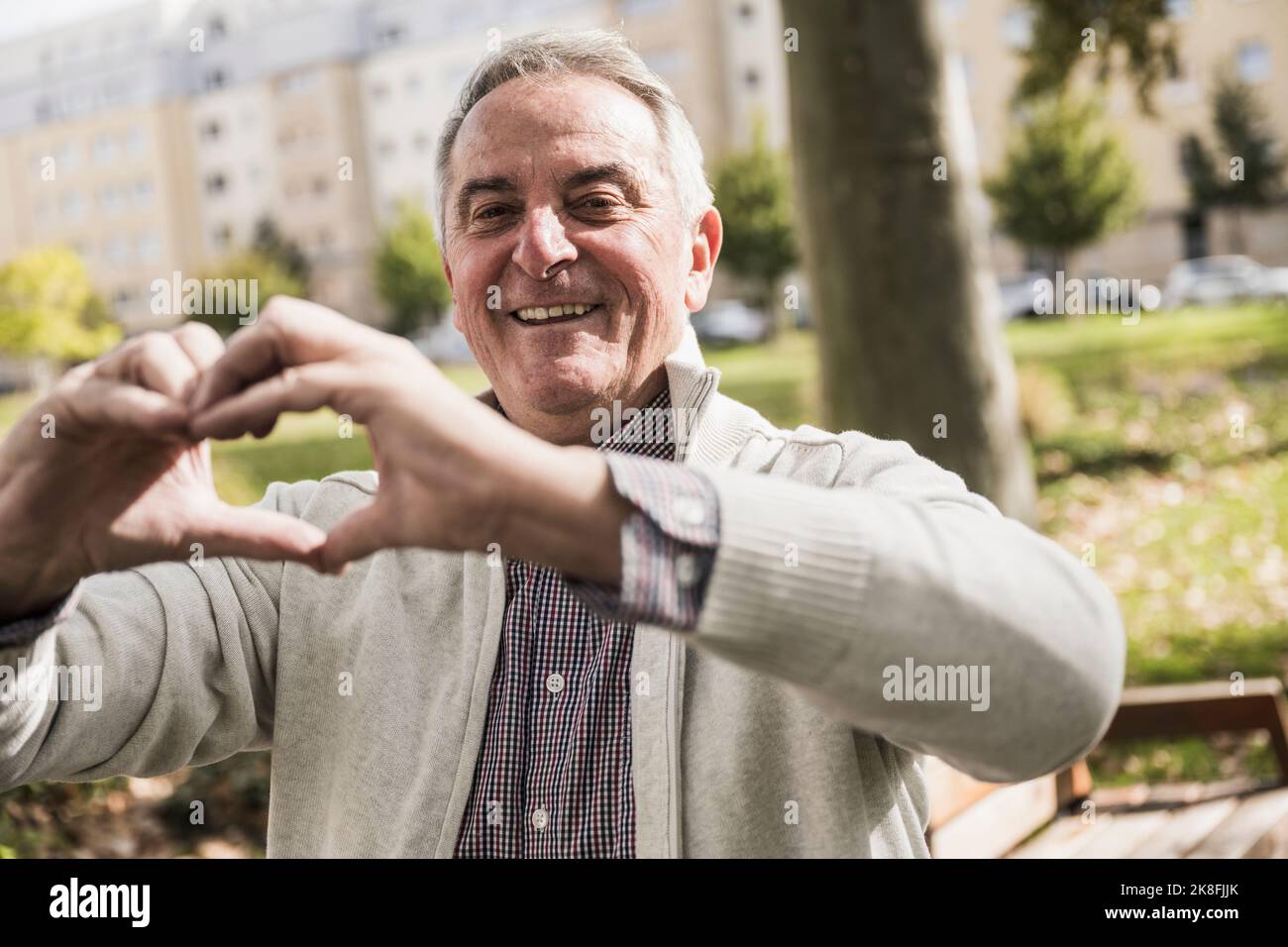 Smiling senior man making heart shape with hand Stock Photo