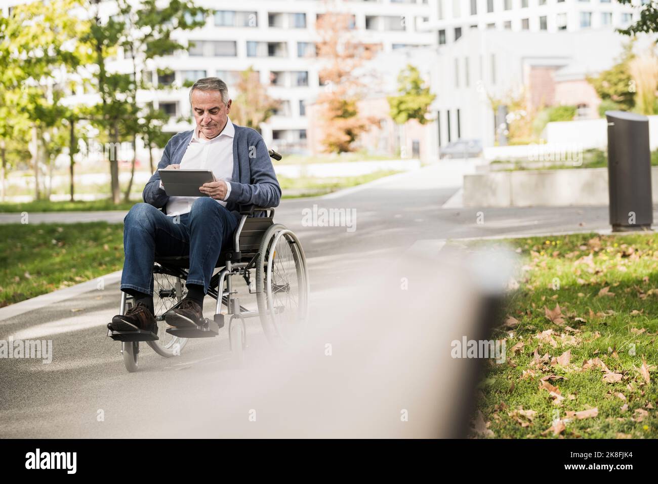 Senior man using tablet PC sitting on wheelchair Stock Photo