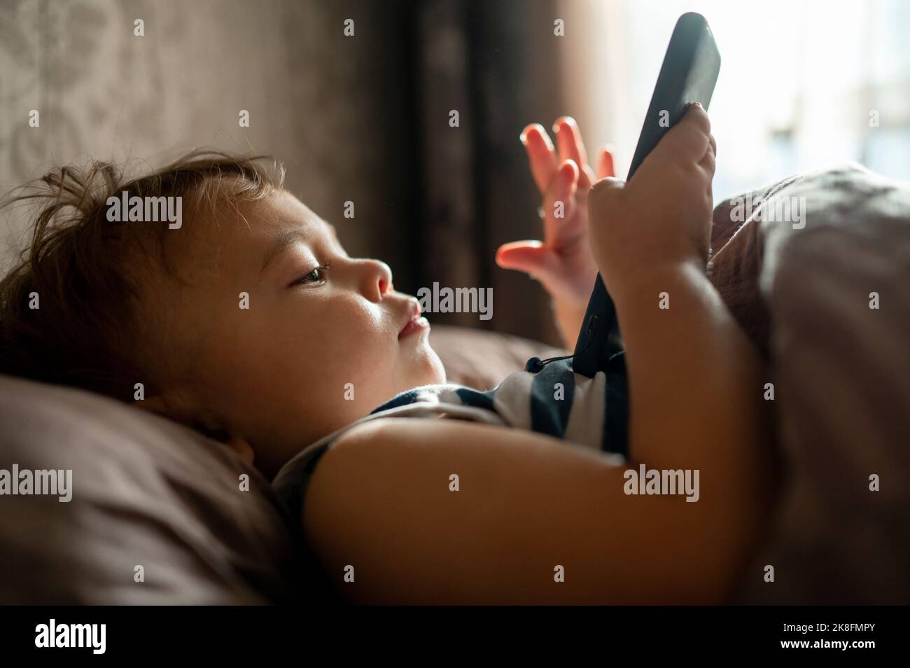 Baby boy using mobile phone lying in bed Stock Photo